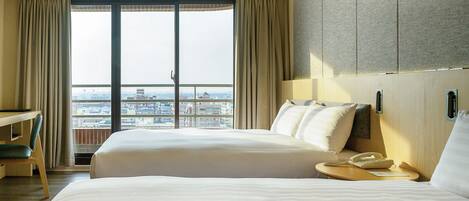 A hotel room with two beds, a desk, and a view of the cityscape.