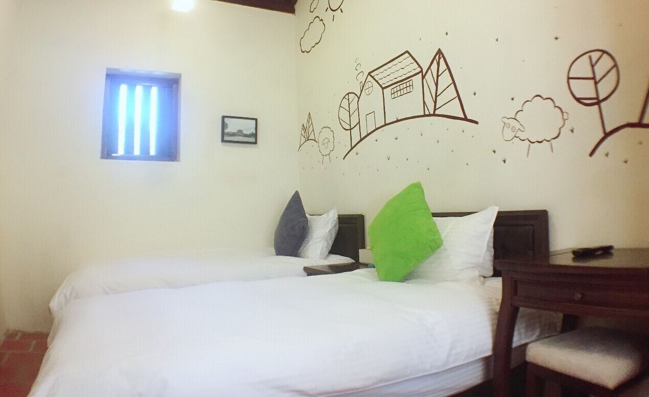 A bedroom with two beds, a small window, and a wall decorated with simple line drawings.
