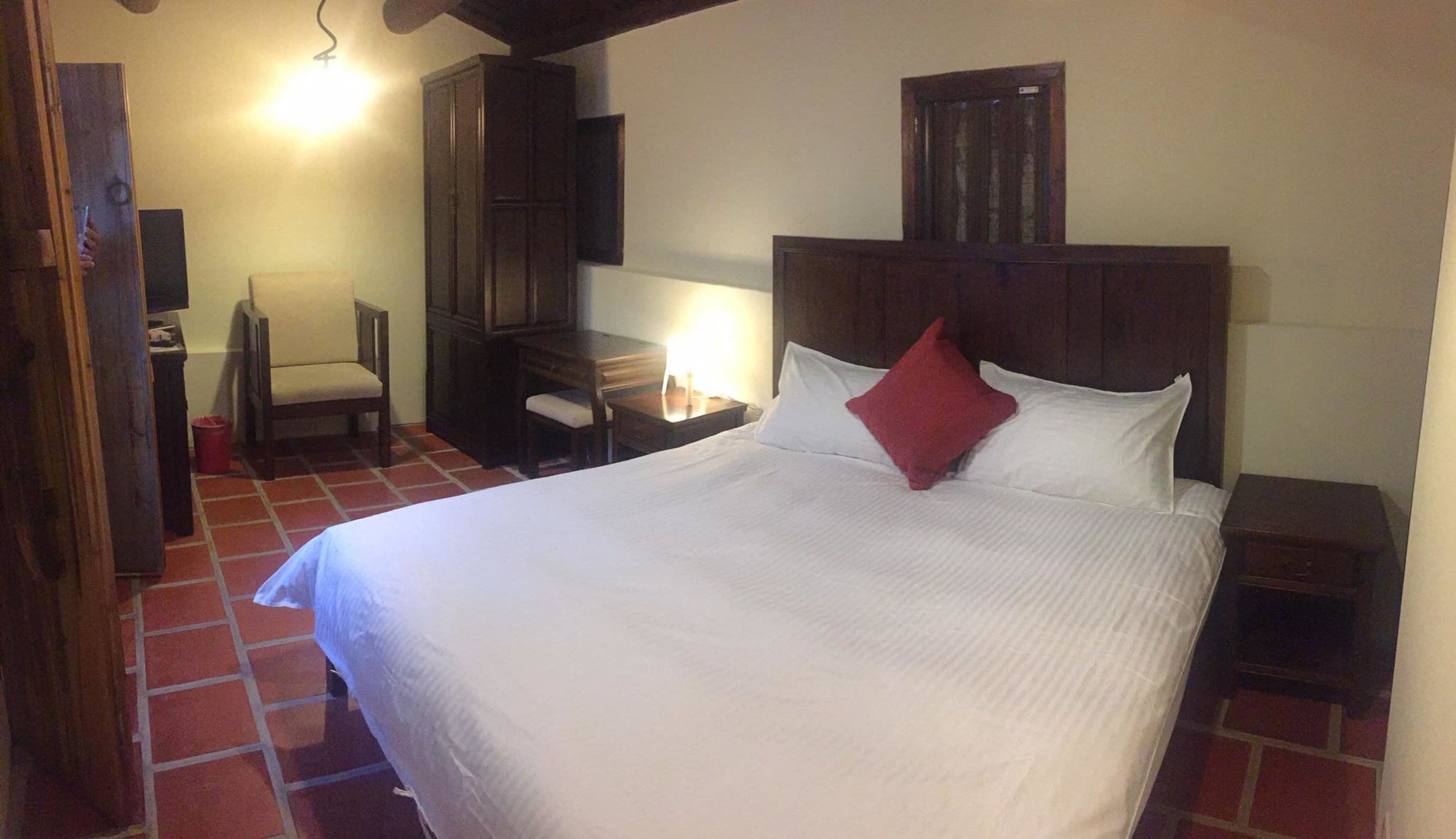 Une chambre d’hôtel avec un grand lit, une tête de lit en bois, un bureau avec une chaise et une armoire.