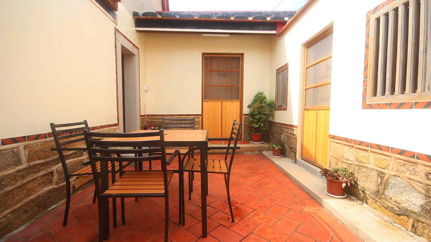 A courtyard with a wooden table and chairs, potted plants, and a door.