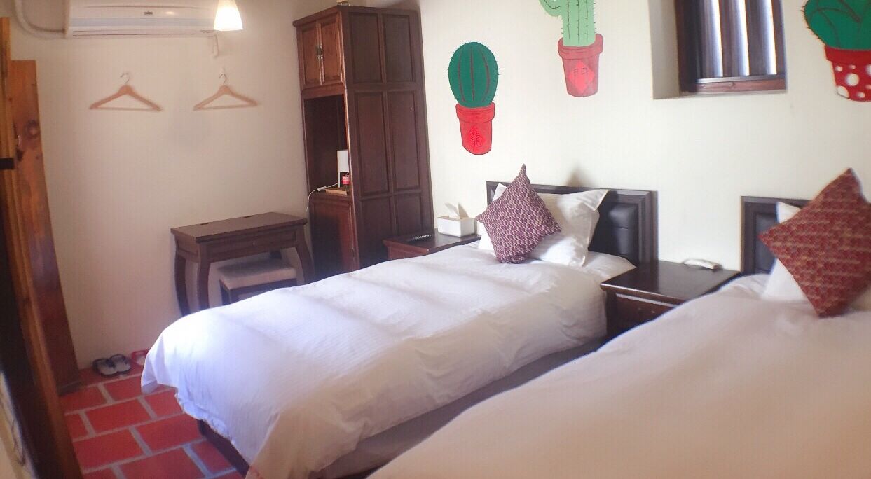 Une chambre d’hôtel avec deux lits, une armoire, un bureau et des éléments de décoration murale, dont un cactus.