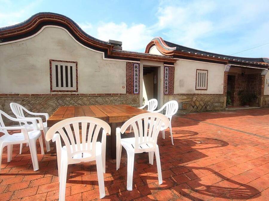 Un edificio con fachada curva, sección inferior de ladrillo y tejado de tejas. Hay una mesa con sillas en frente.