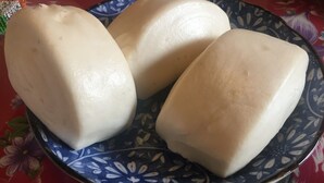 Une assiette bleue à motifs sur laquelle sont disposés trois petits pains blancs.