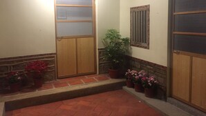 Un couloir avec une porte en bois, une fenêtre grillagée et des plantes en pot.
