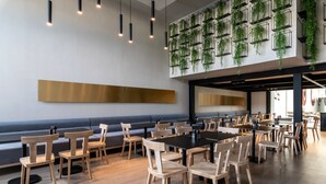 Un comedor moderno con mesas y sillas de madera, un banco largo y plantas colgantes en la pared.