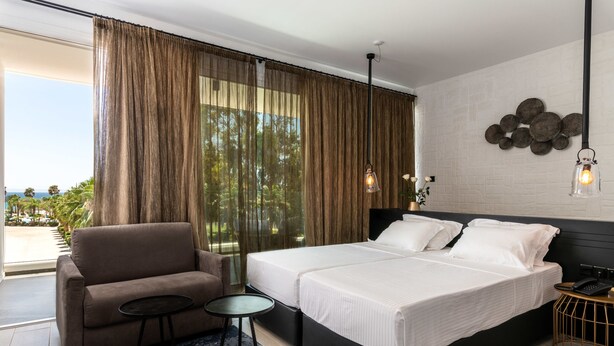Habitación de hotel moderna con una cama grande, un sofá, una mesita y vistas al exterior.