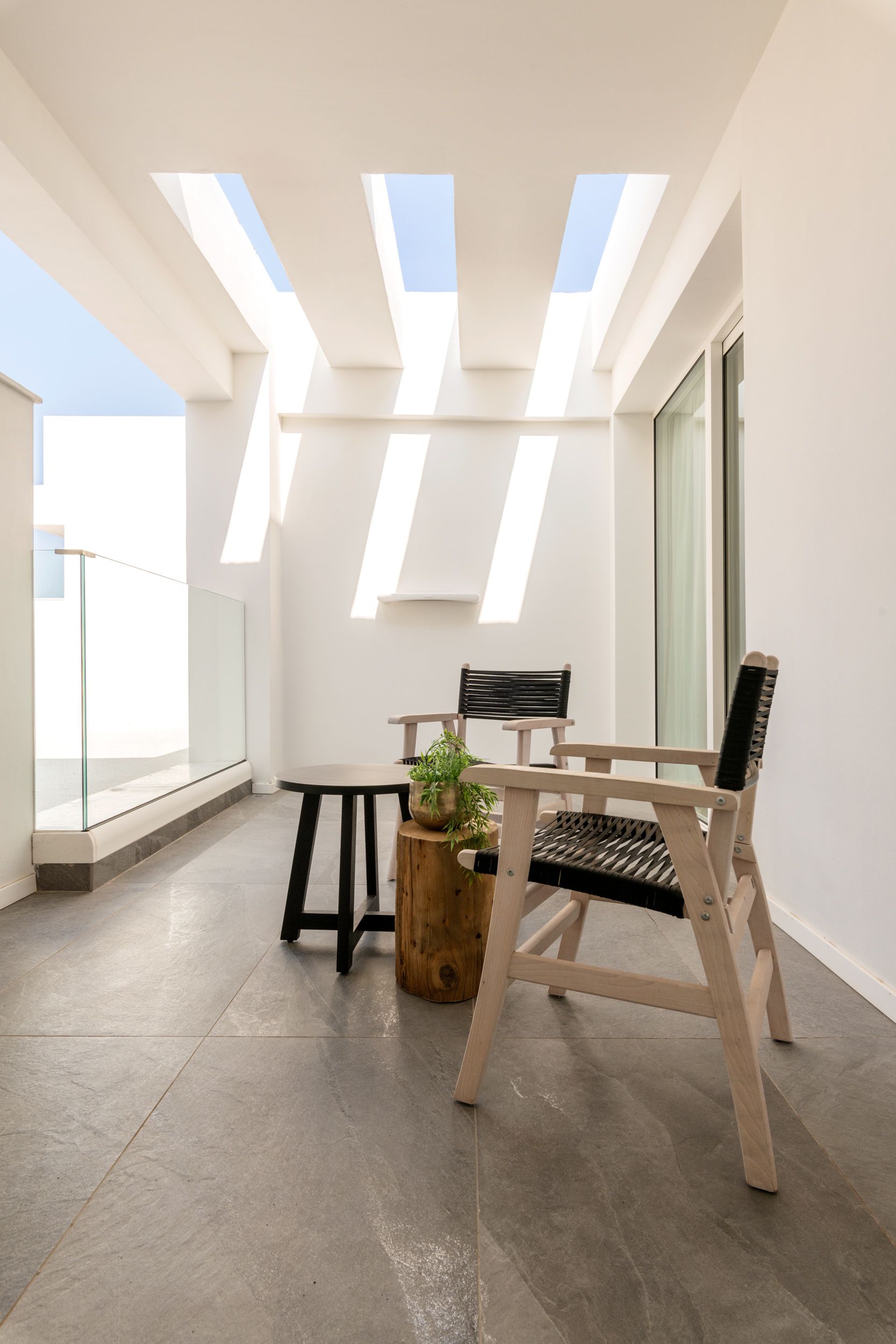 Un balcon moderne avec une balustrade en verre, une chaise en bois, une petite table et un pot de fleurs.
