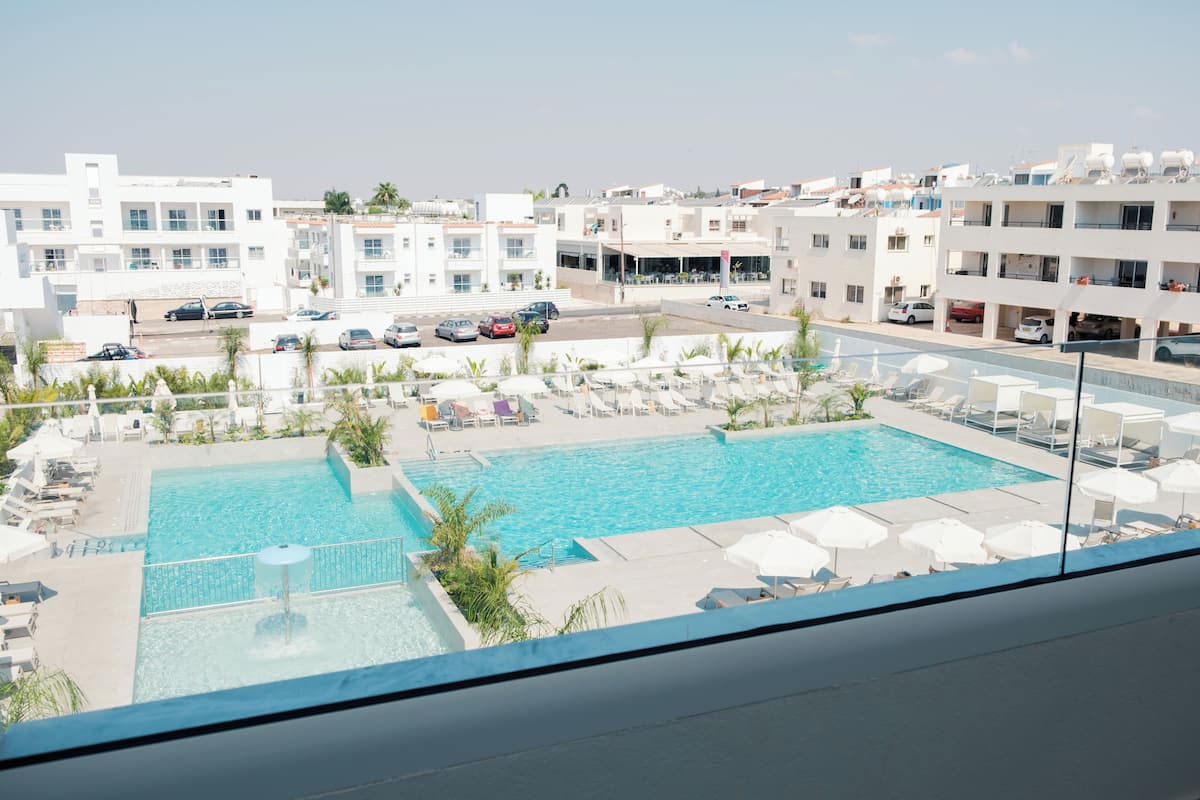 Un área de piscina en la azotea con sillones de descanso y sombrillas, rodeada de edificios modernos.