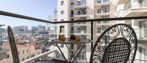 Un balcon avec une table et des chaises, donnant sur un paysage urbain avec des bâtiments modernes.