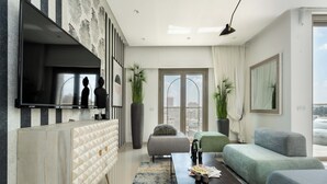 Uma sala de estar moderna com televisão de tela plana, um sofá, uma mesa de centro e uma janela grande com vista para a cidade.