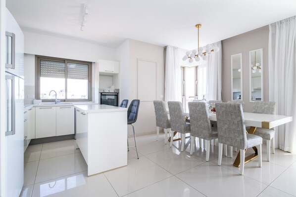 Una cocina moderna con armarios blancos, una isla central y un comedor con sillas tapizadas en gris y una mesa blanca.