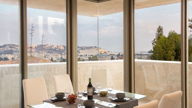 Espaço de jantar com mesa posta para dois, janelas amplas com vista para a cidade e colinas.