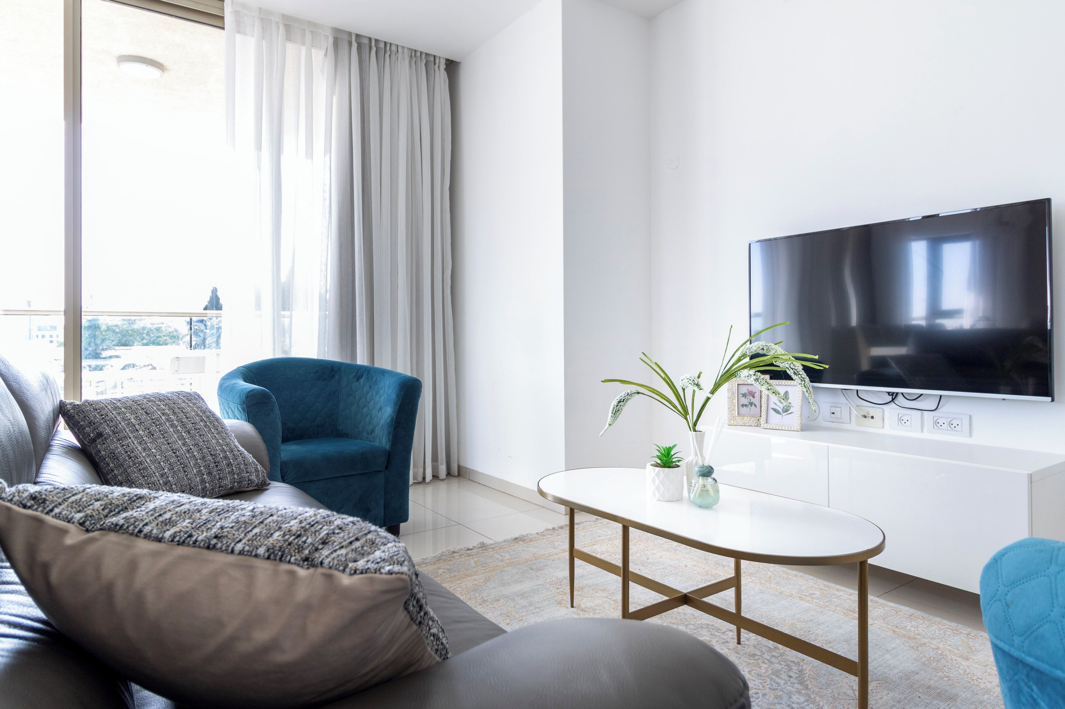 A modern living room with a sofa, a blue armchair, a coffee table, and a TV mounted on a white cabinet.