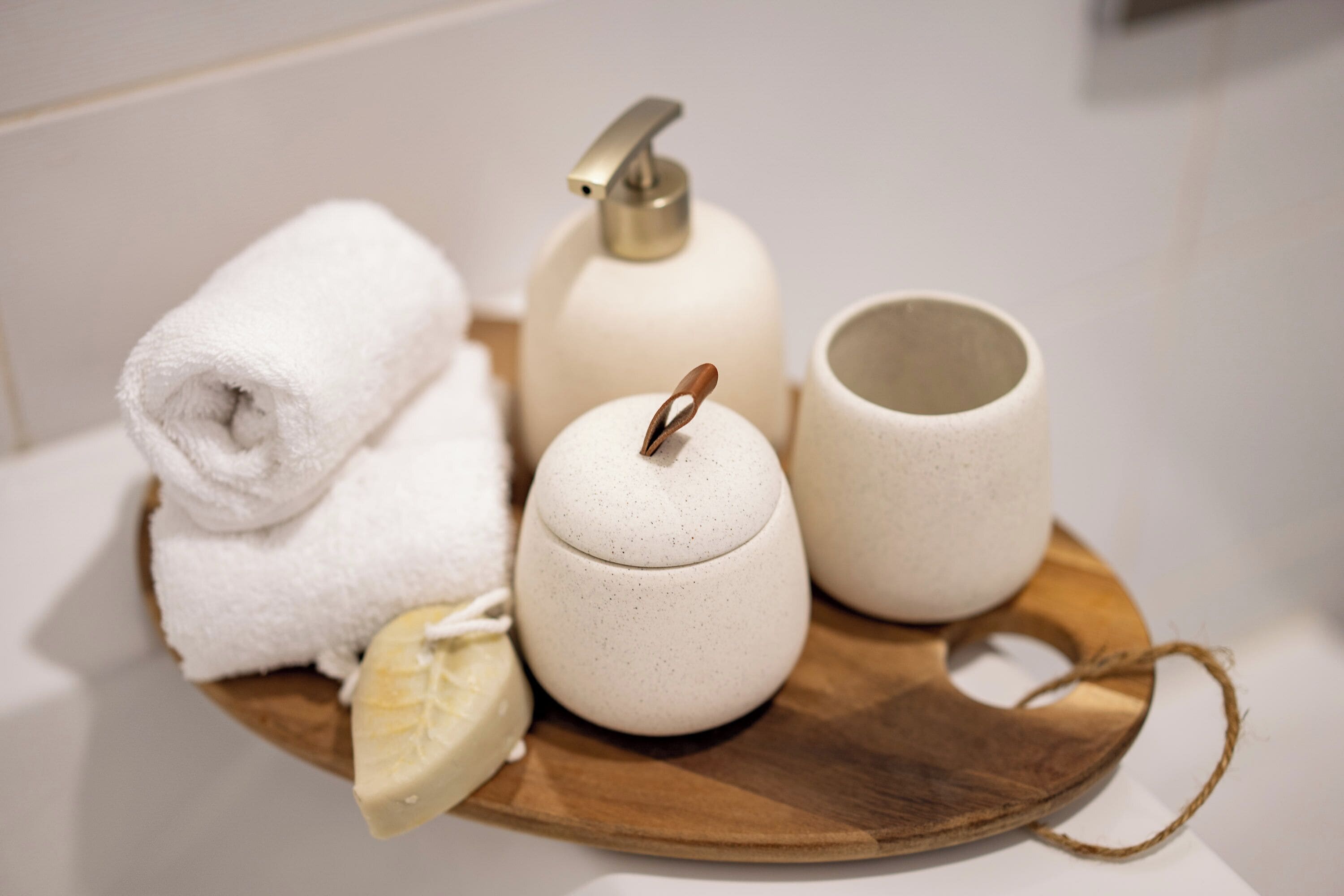A wooden tray with a rolled white towel, a soap dispenser, a soap bar, and a ceramic mug.
