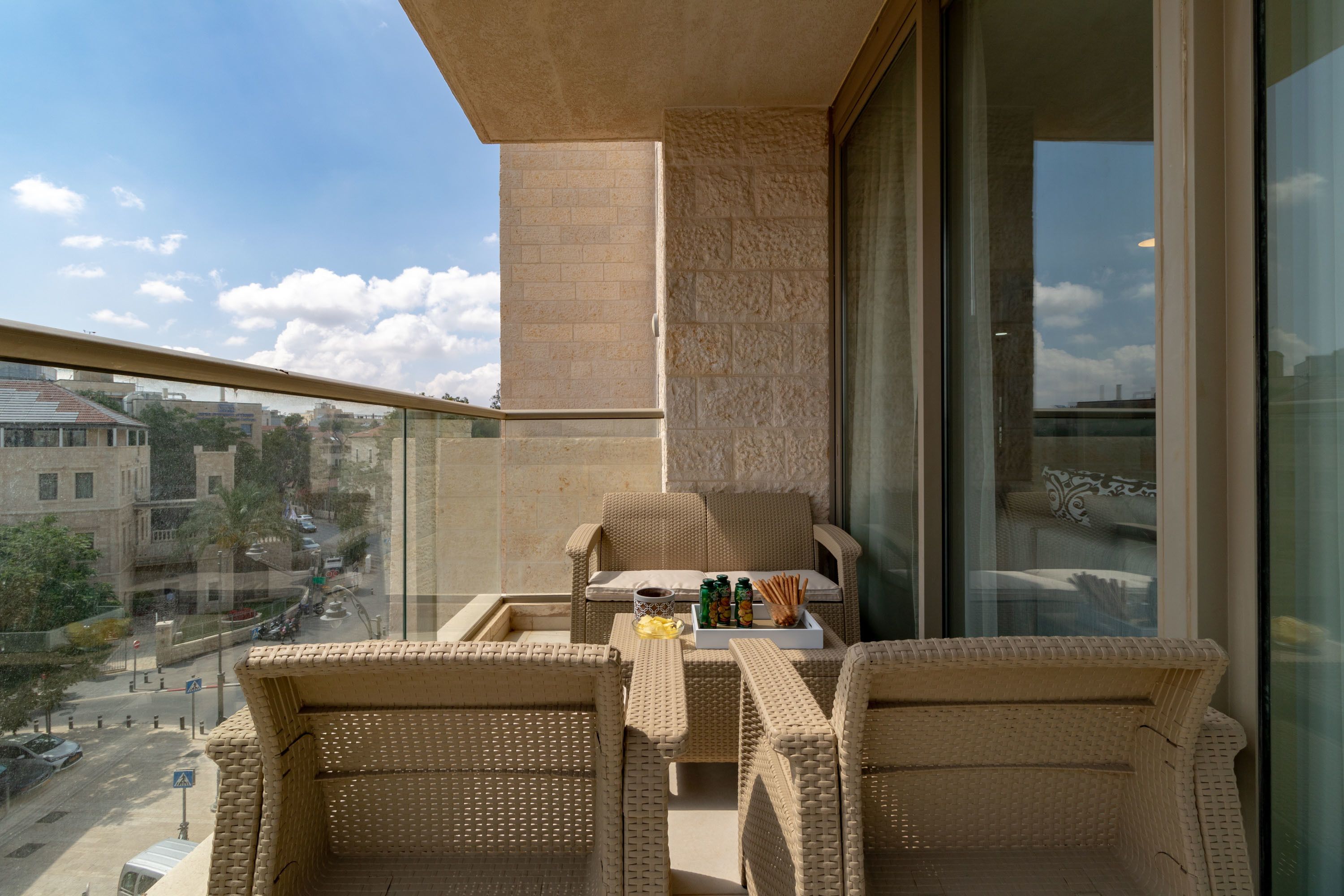 Un balcón con mobiliario de mimbre, una mesa con botellas y vistas a la ciudad.