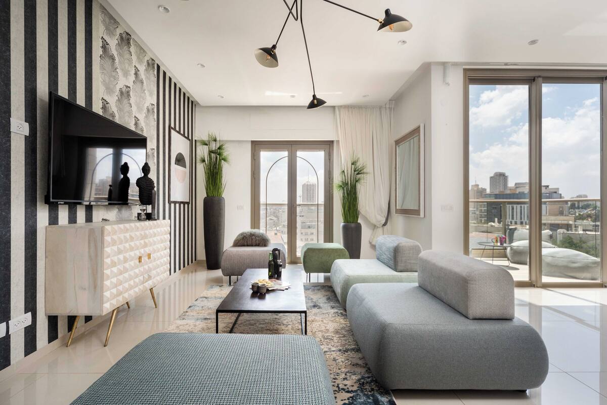 Ein modernes Wohnzimmer mit großem Fernseher, Sofas, einem Couchtisch und Blick auf die Stadt.