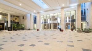 Um hall amplo, com pé direito alto, grandes janelas e piso de azulejos.