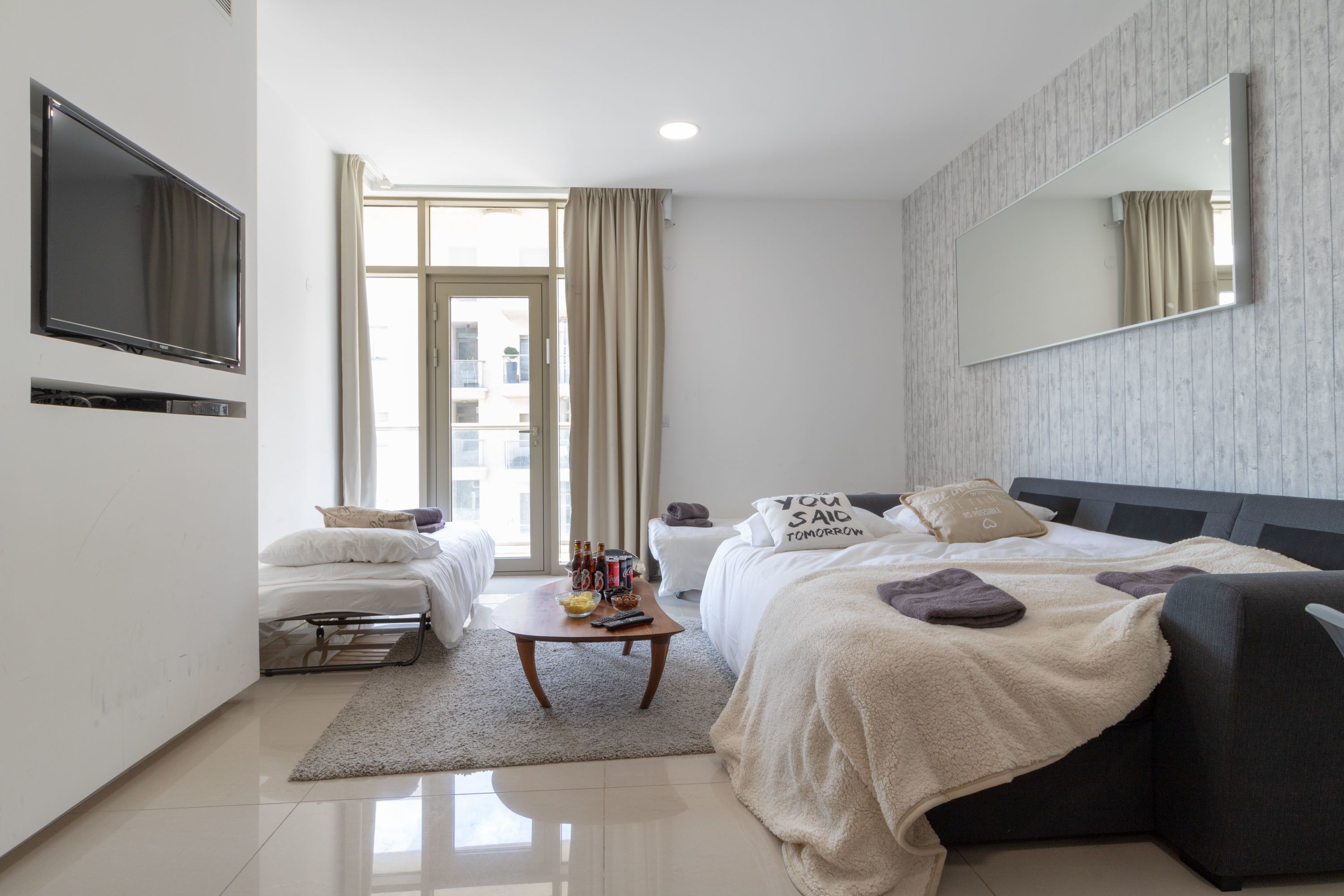 Een moderne hotelkamer met een groot bed, een slaapbank, een televisie en een groot raam met gordijnen.