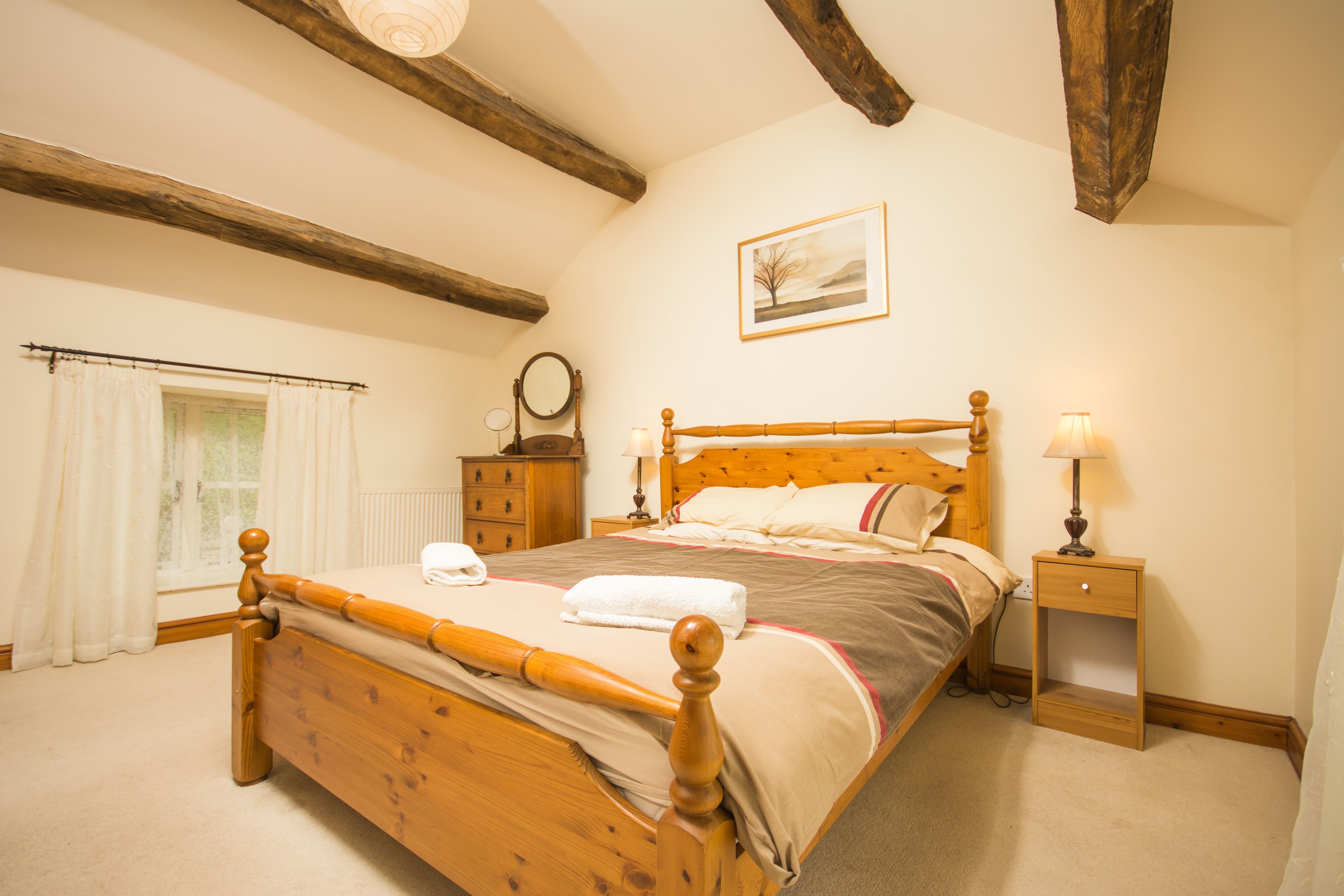 A bedroom with a wooden bed, a nightstand, a lamp, a window with curtains, and a painting on the wall.