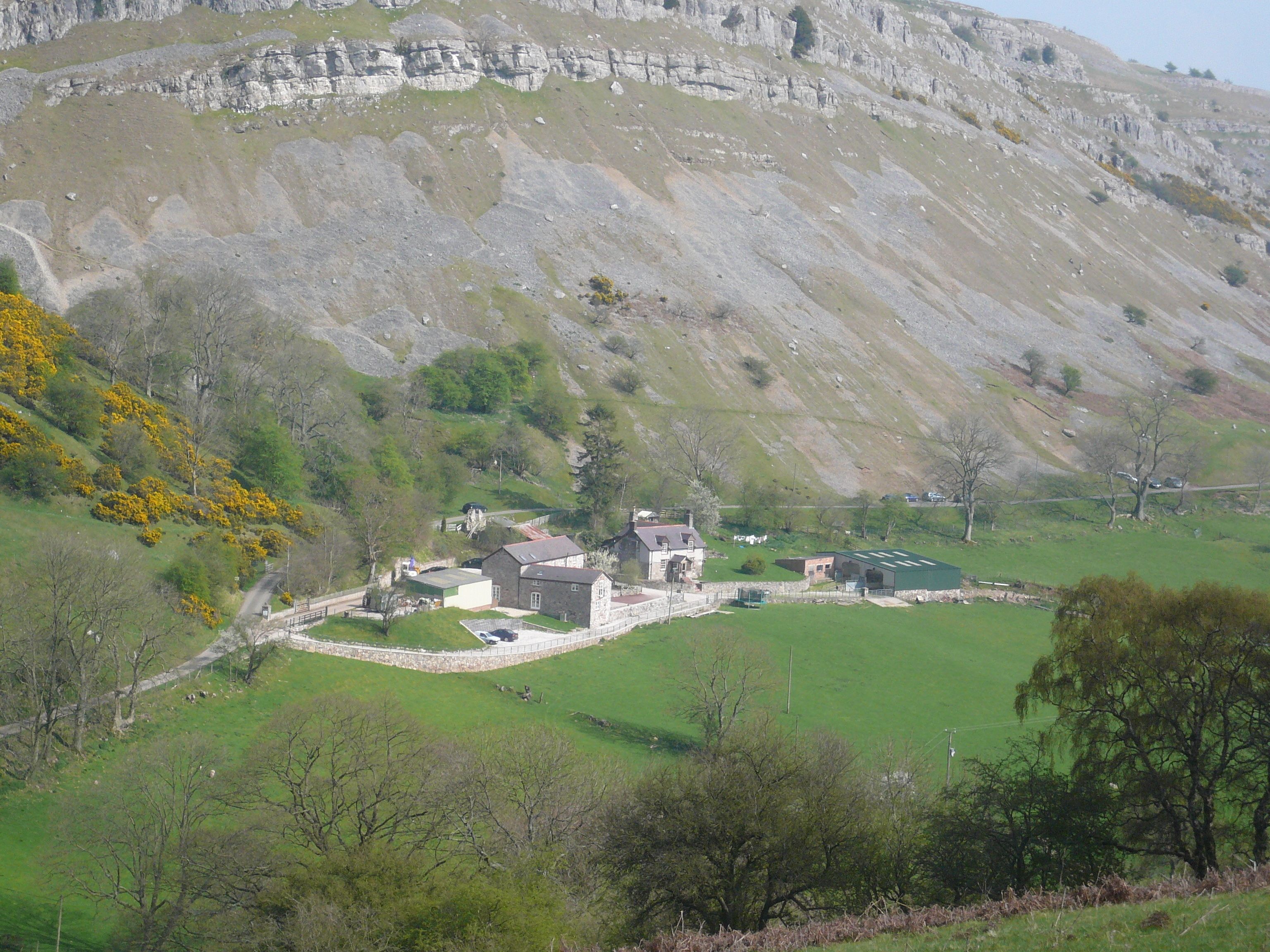 A rural property with a stone house, a green field, and a mountainous backdrop.