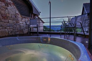 Un jacuzzi con vistas a las montañas, paredes de piedra y dos sillas en una terraza.