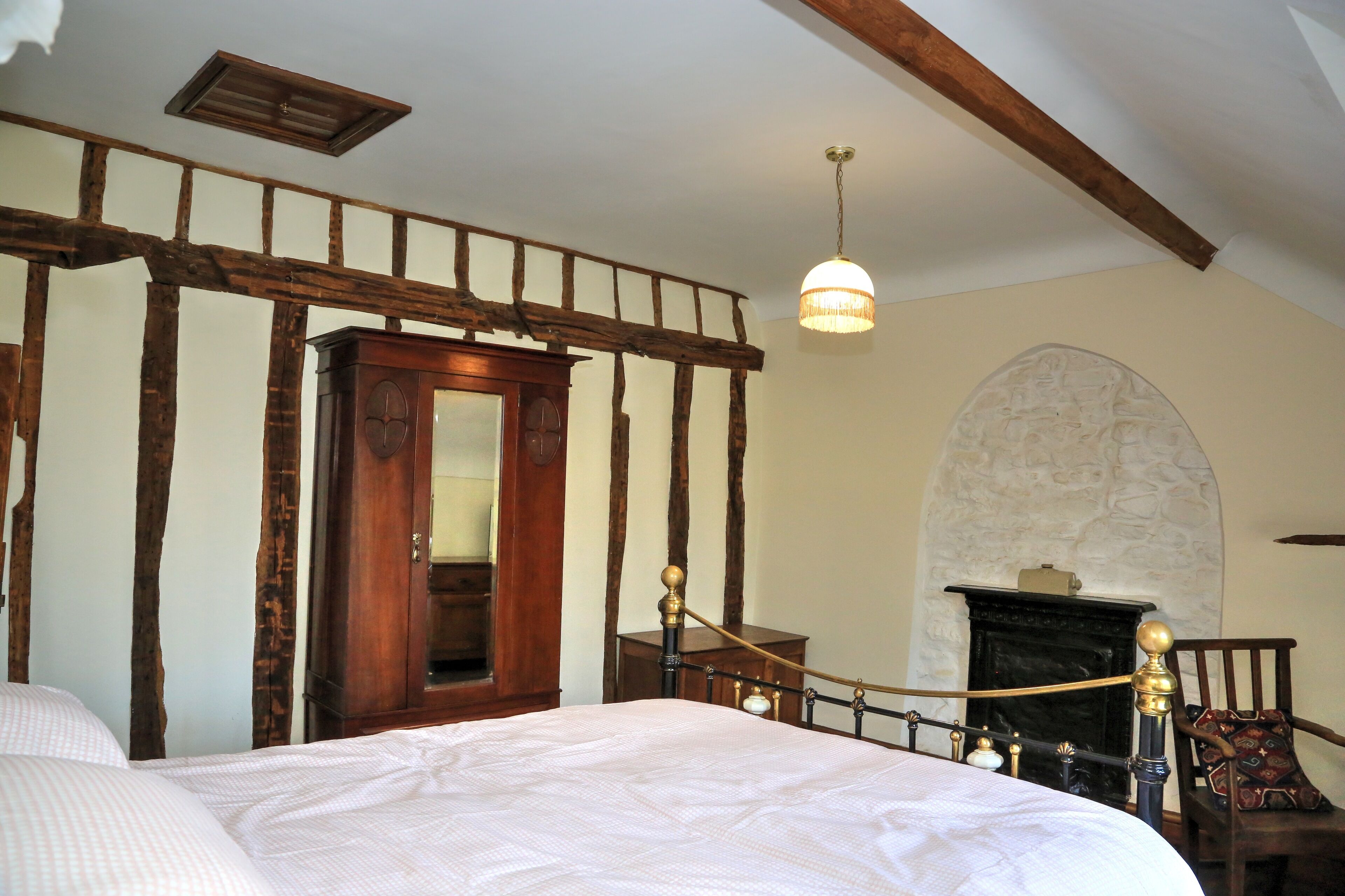 Une chambre avec un grand lit, des poutres apparentes, une cheminée et un lustre.