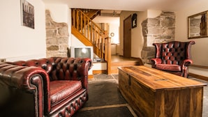 A living room with a wooden coffee table, two red leather sofas, a stone wall, and a staircase leading to another room. - Panorama Cottages (Llangollen)
