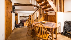 A wooden dining table with chairs, a staircase, and a stone wall in the background. - Panorama Cottages (Llangollen)