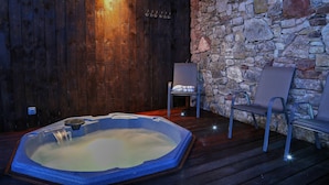 A hot tub with a stone wall and wooden paneling, two chairs, and a small table. - Panorama Cottages (Llangollen)