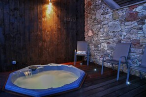 A hot tub with a stone wall and wooden paneling, two chairs, and a small table. - Panorama Cottages (Llangollen)