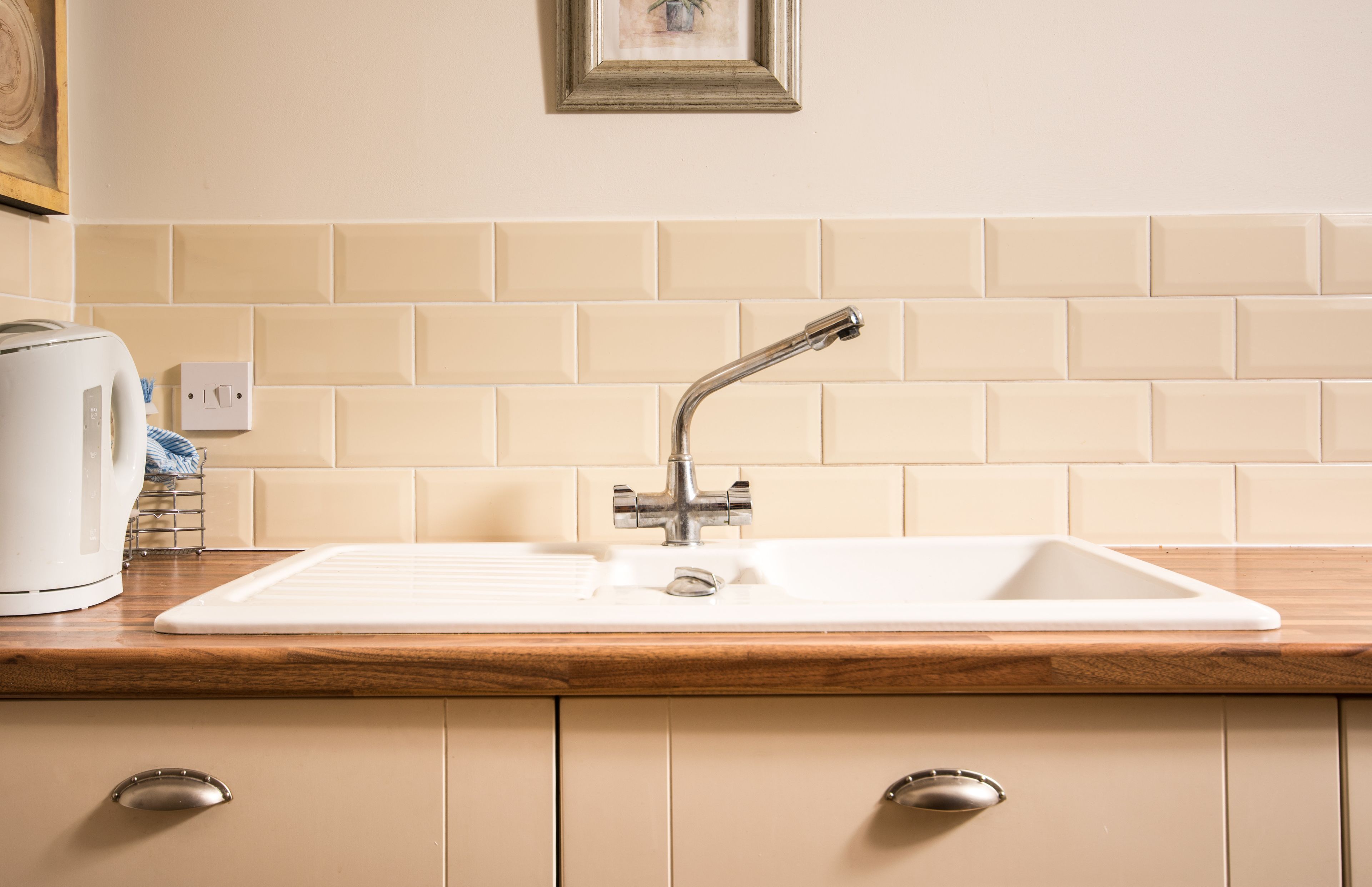 A kitchen with a white sink, wooden countertop, and beige tiles.