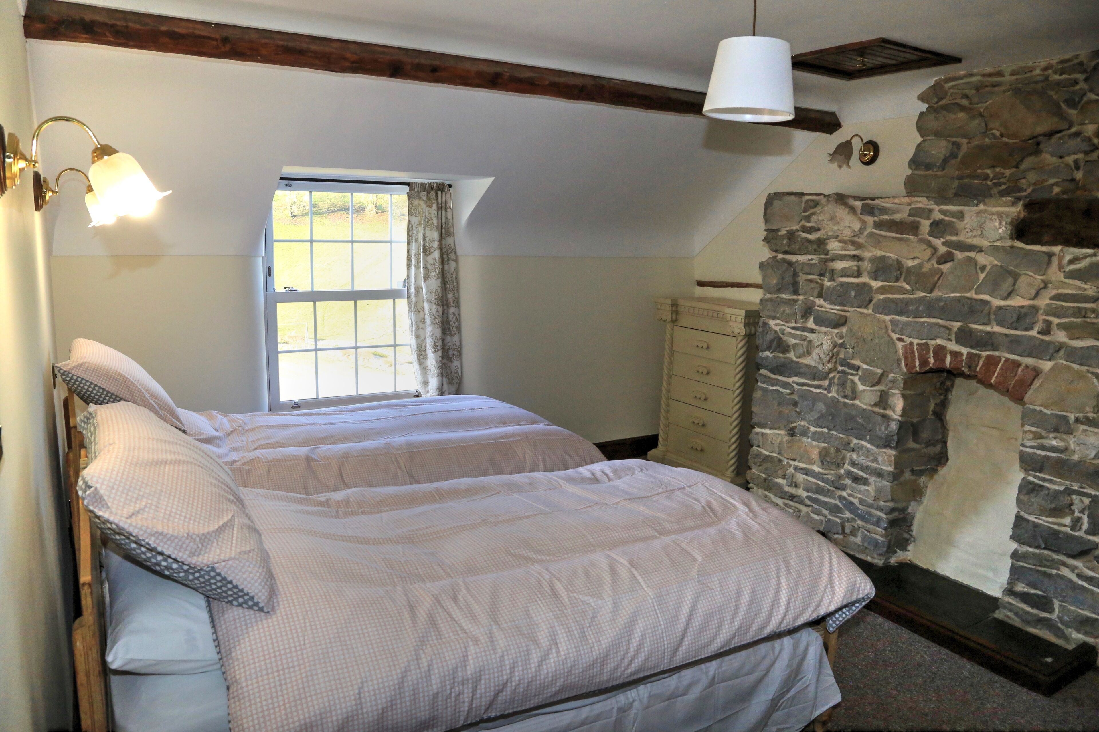 A bedroom with a stone fireplace, a window with curtains, and a bed with a headboard.