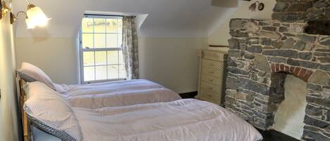 A bedroom with a stone fireplace, a window with curtains, and a bed with a headboard.