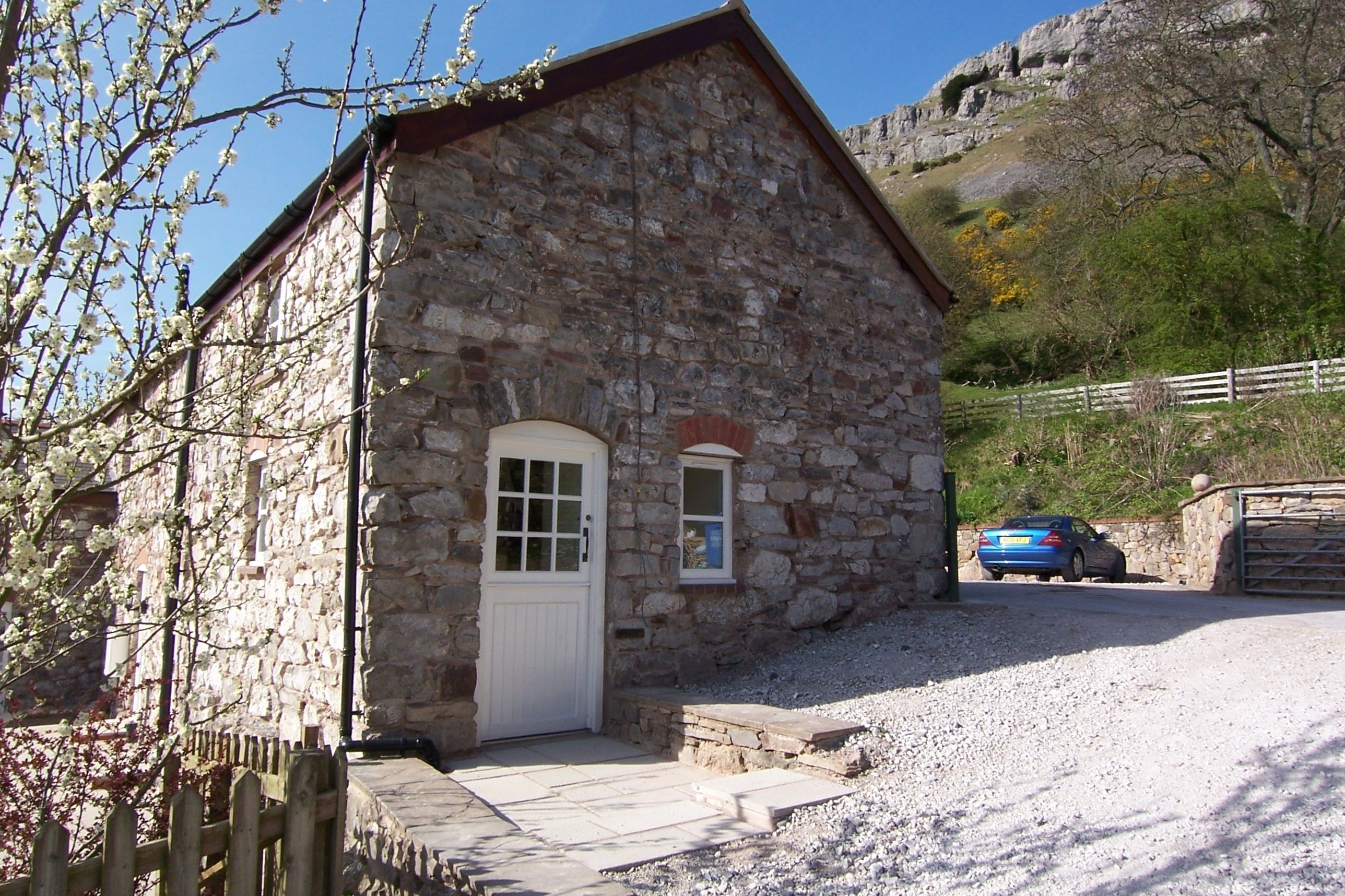 A stone building with a white door and window, a gravel driveway, and a parked car.
