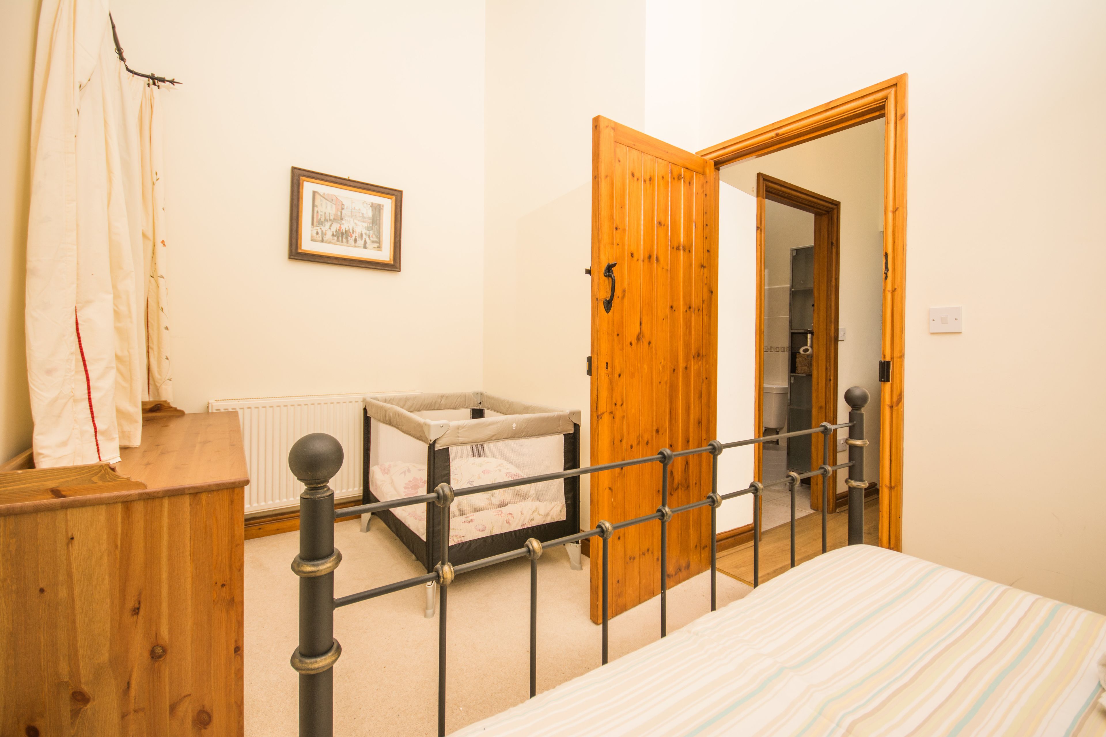A bedroom with a wooden bed frame, a single bed, a wooden wardrobe, a small window, and a door leading to another room.