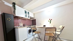 Een compacte keuken met een wasmachine, een eettafel met stoelen en een kleine plant aan de wand.