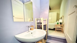 Een badkamer met een wit wastafelmeubel, een spiegel en een houten plank. Er is een trap die naar een andere kamer leidt.