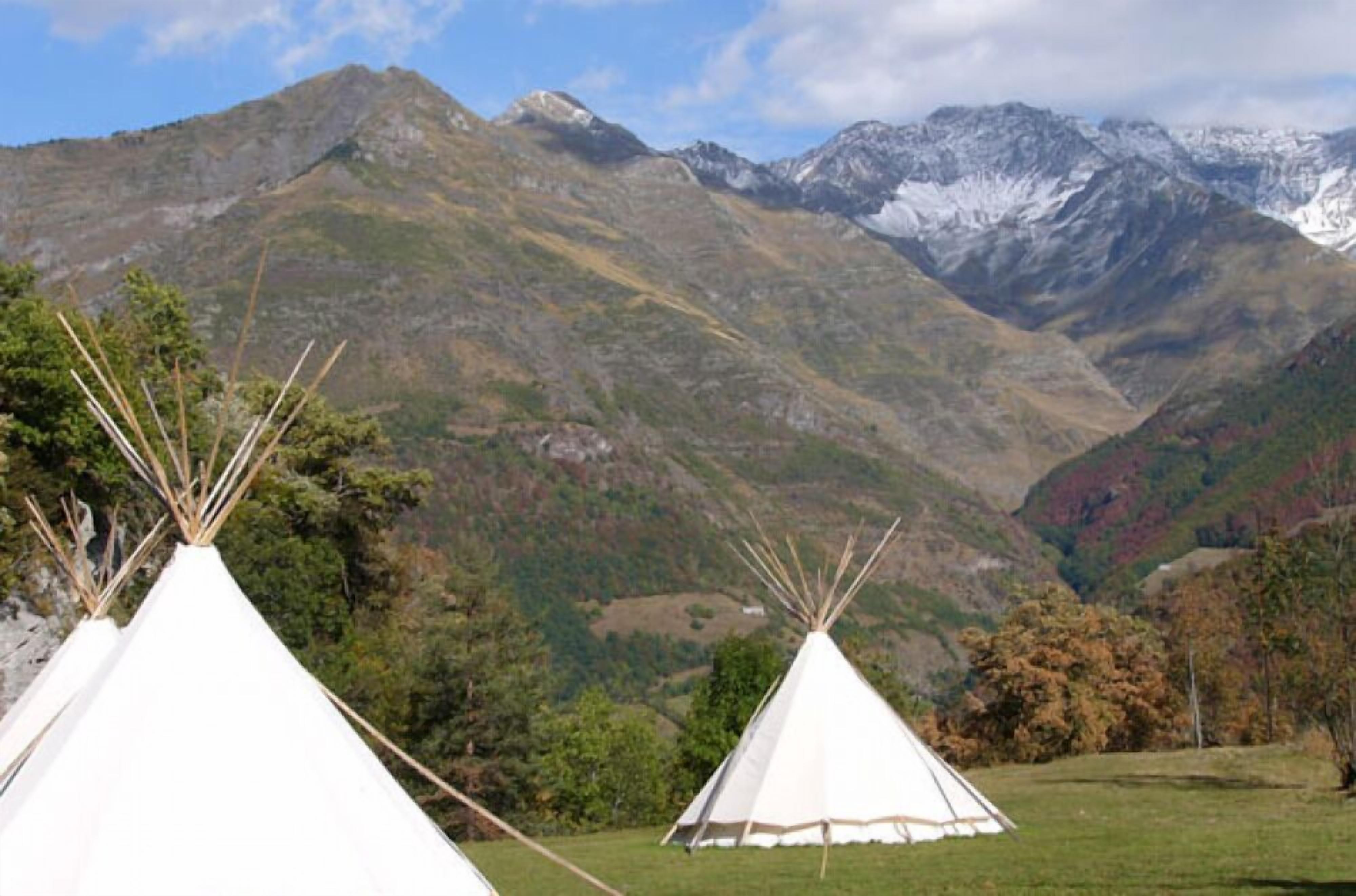 A mountainous landscape with white teepees in a grassy field.