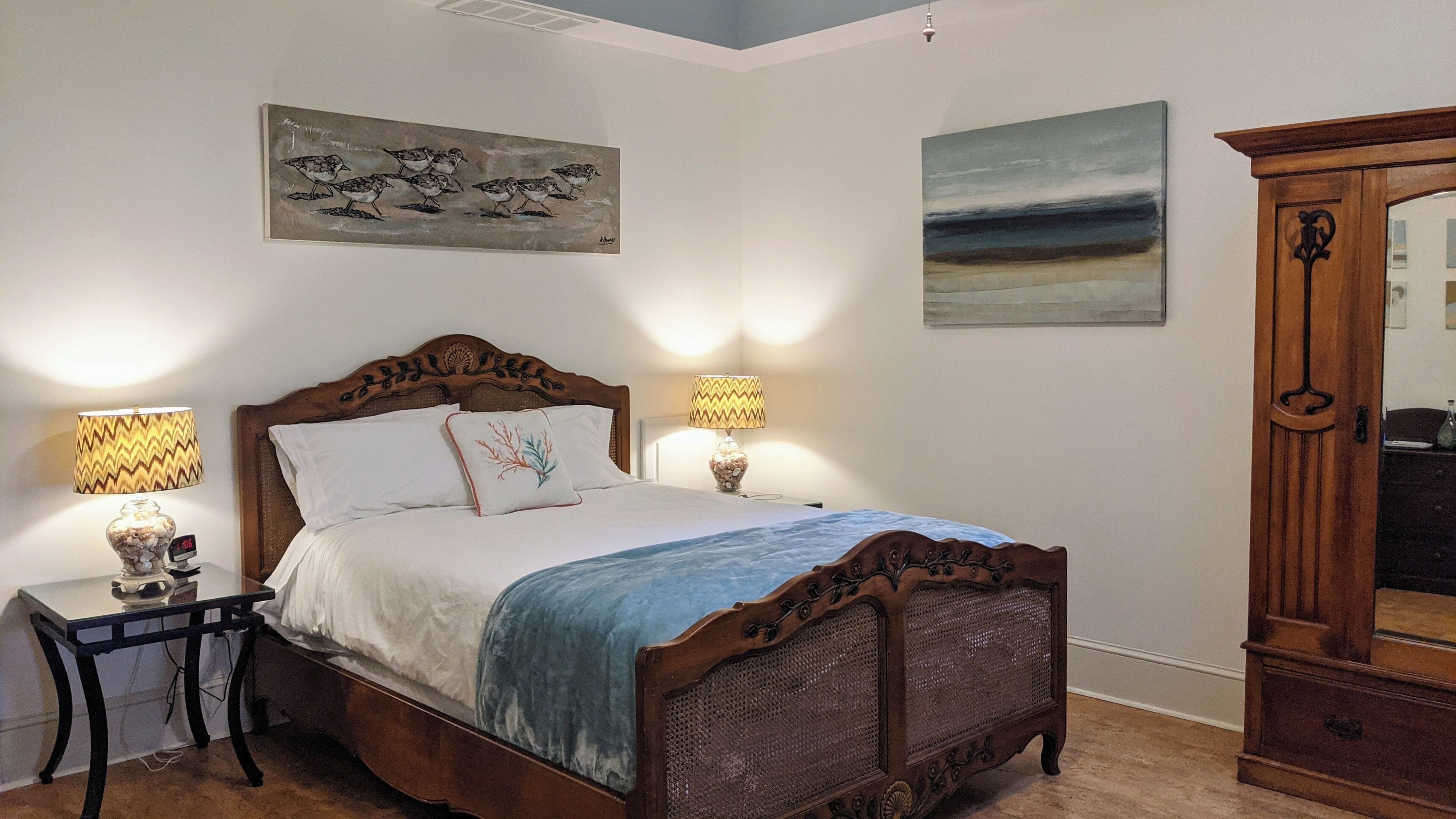 Een slaapkamer met een houten bed, twee bedlampen, een nachtkastje, een spiegel en twee wanddecoraties.
