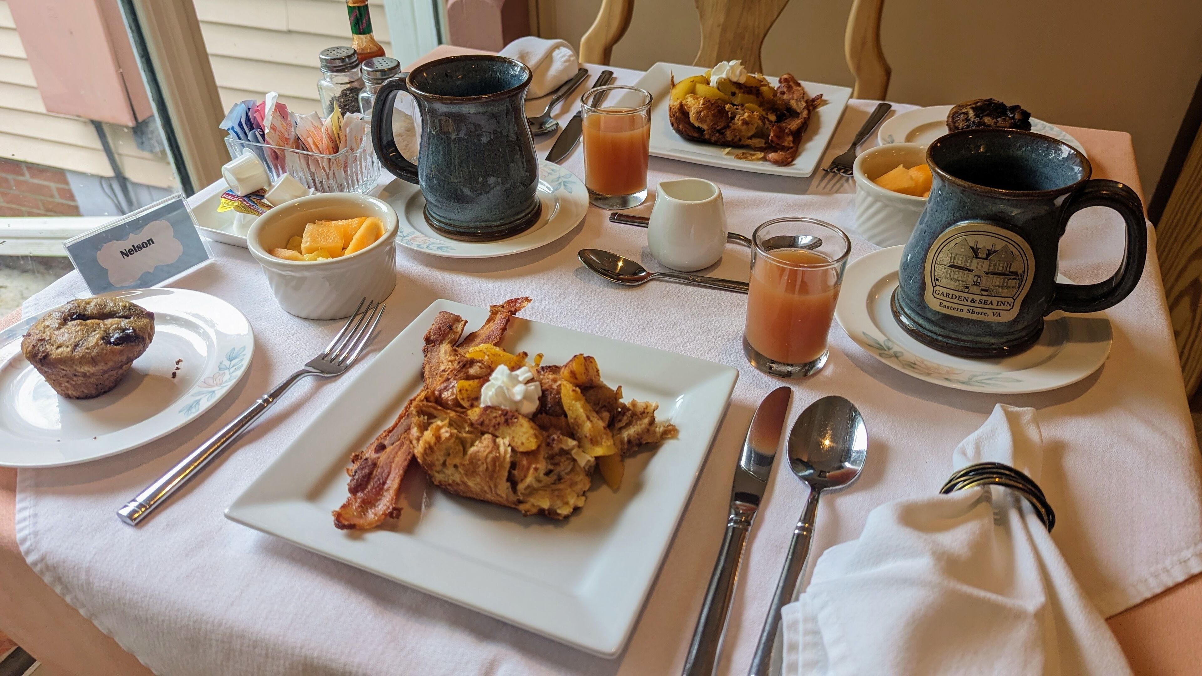 A breakfast table with plates of food, a mug, and various condiments.