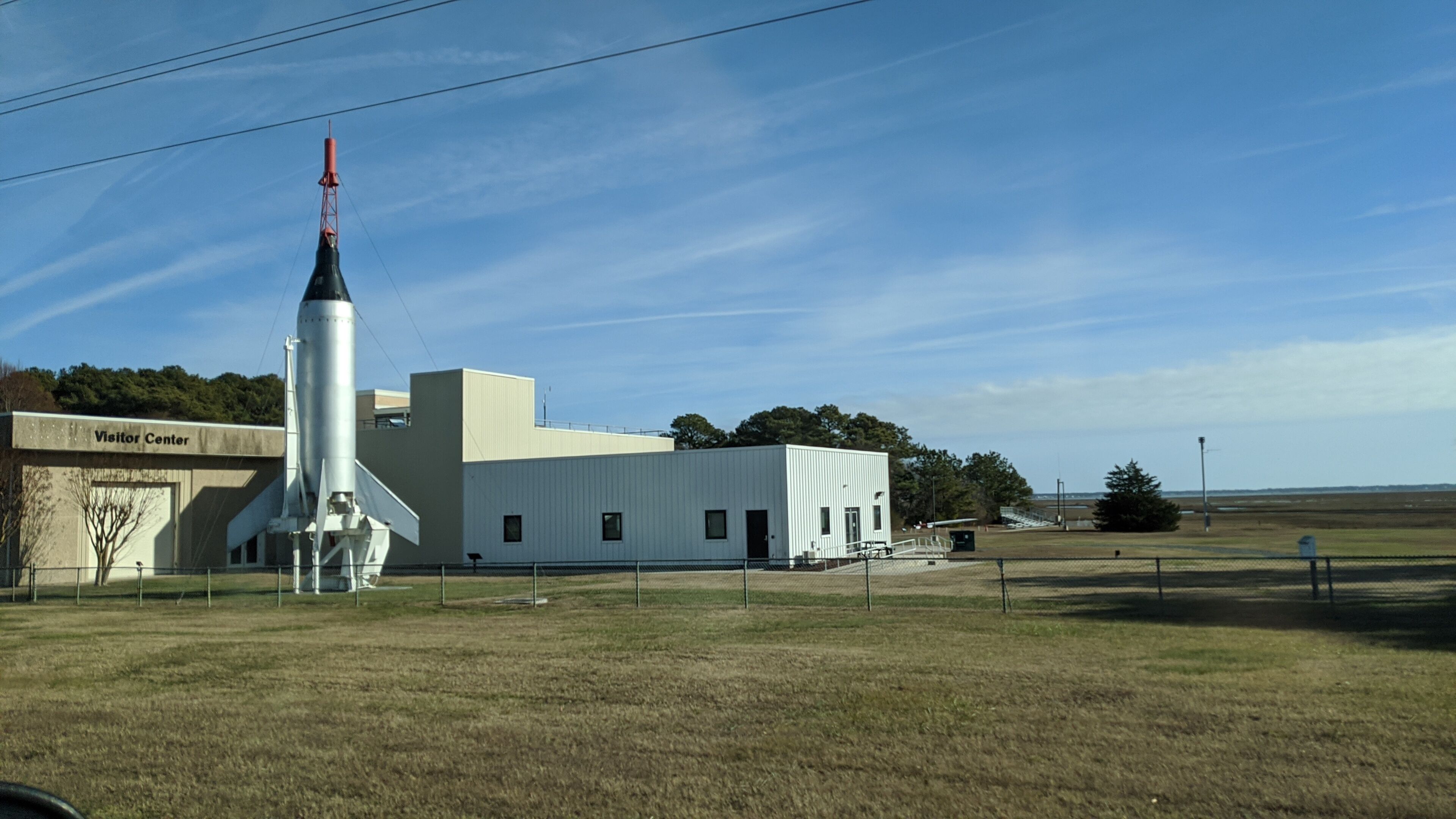 A rocket on display at a visitor center with a grassy field and a clear sky in the background.