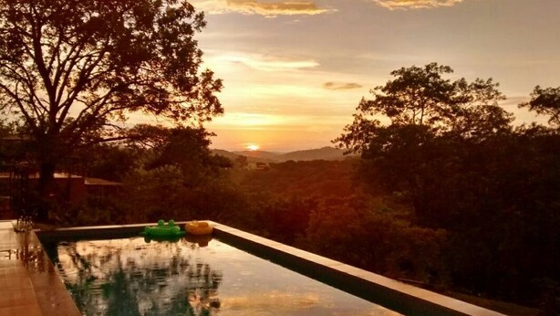 A swimming pool with a sunset view, surrounded by trees and hills.