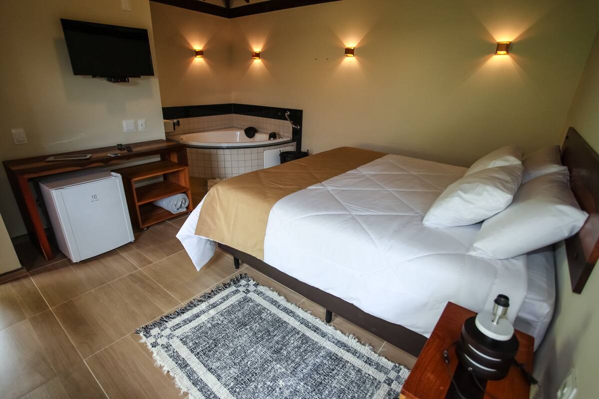 A hotel room with a bed, a small refrigerator, a bathtub, and a TV mounted on the wall.