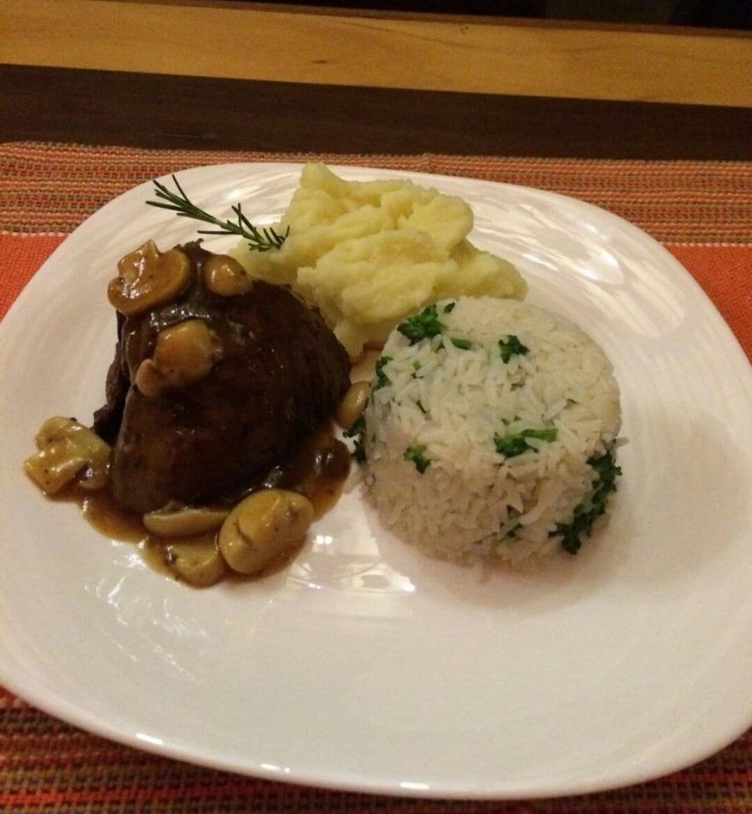 A plate with a beef steak, mashed potatoes, and rice.