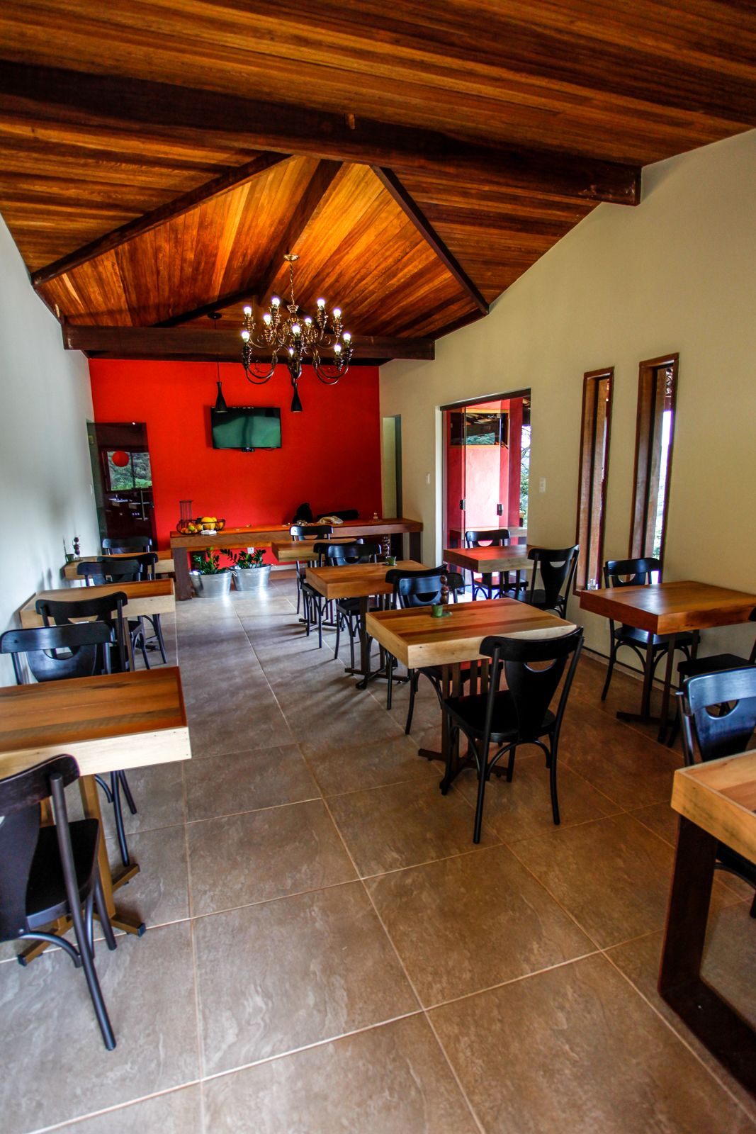 A restaurant with wooden tables and chairs, a red wall, and a chandelier.