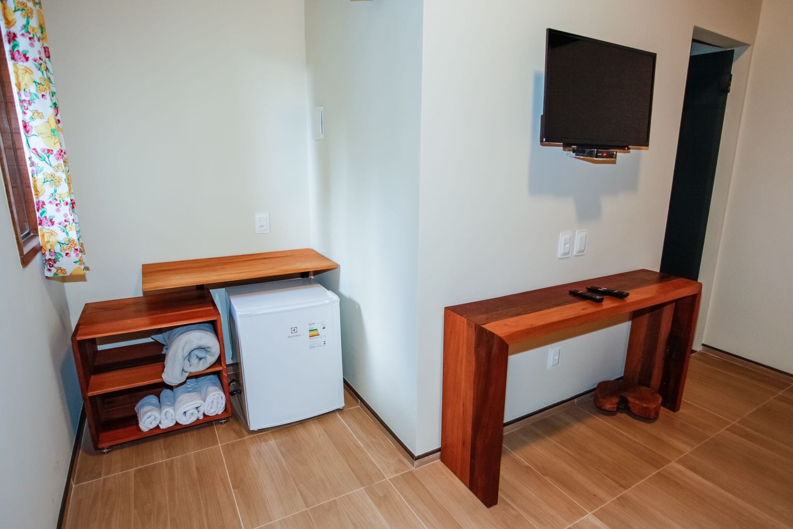 A small room with a wooden table, a white refrigerator, and a TV mounted on the wall.