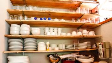 Una cocina con estantes de madera que contienen diferentes utensilios de cocina, como platos, tazones, tazas y cubiertos.