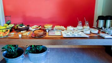 A breakfast buffet with various food items and beverages on a wooden table against a red wall.