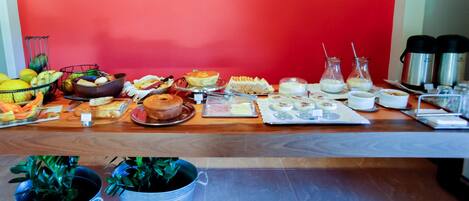 A breakfast buffet with various food items and beverages on a wooden table against a red wall.