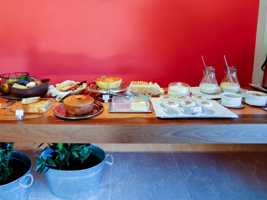 A breakfast buffet with various food items and beverages on a wooden table against a red wall.